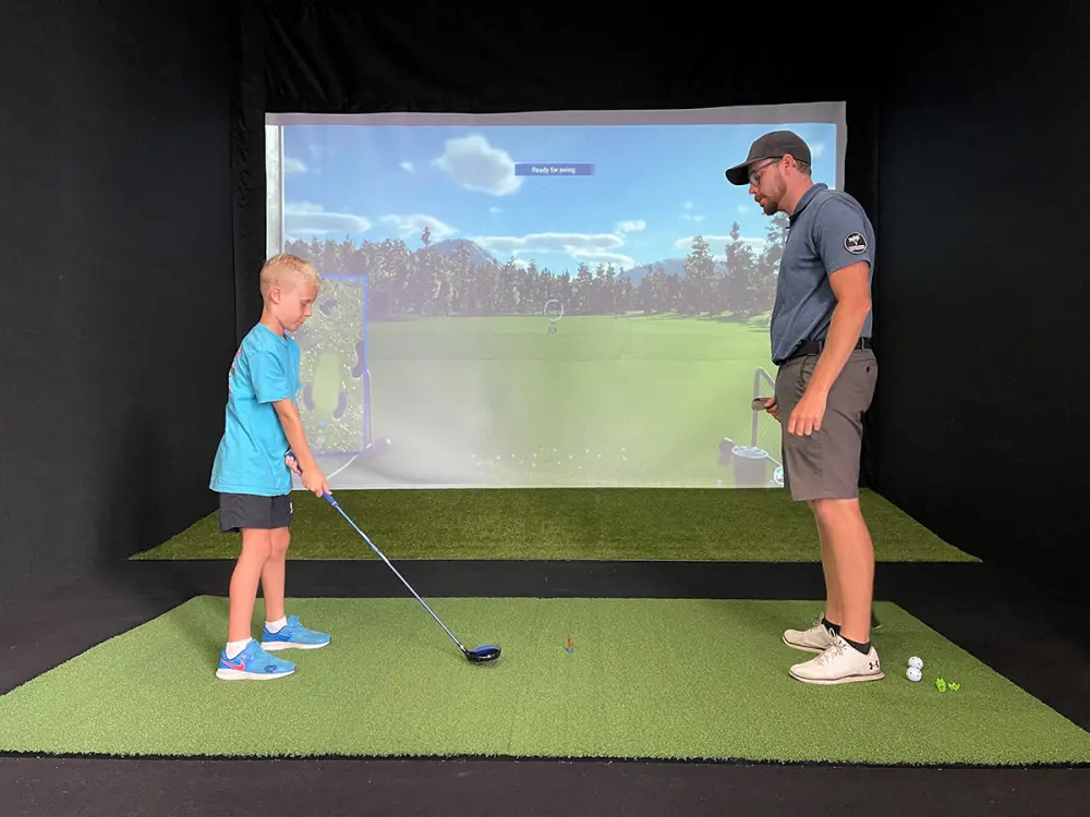 A coach working with a junior player in front of the simulator screen.