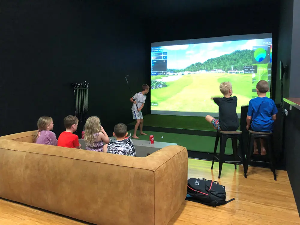 Kids on the couch watching a mate tee off into the simulator screen.